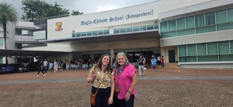 Two women standing in front of Anglo-Chinese School with brick courtyard and students visible in background