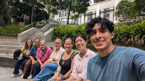 Group of seven people posing on outdoor steps in front of ivy-covered buildings, smiling at camera