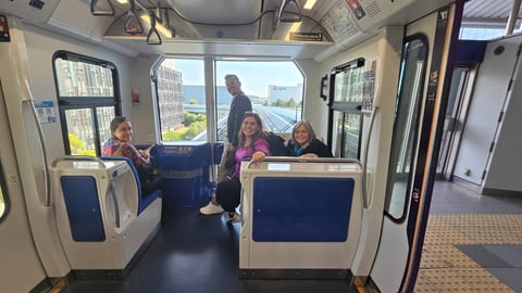Interior of a public transit bus with four passengers seated, showing blue and white seats and large windows