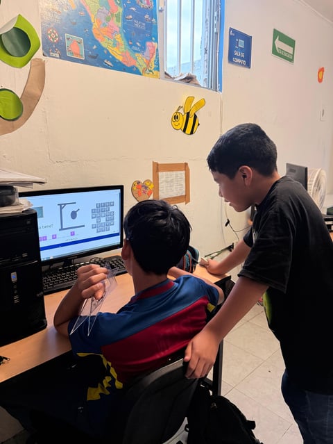 Two students in a classroom working together at a computer displaying design software on the screen.