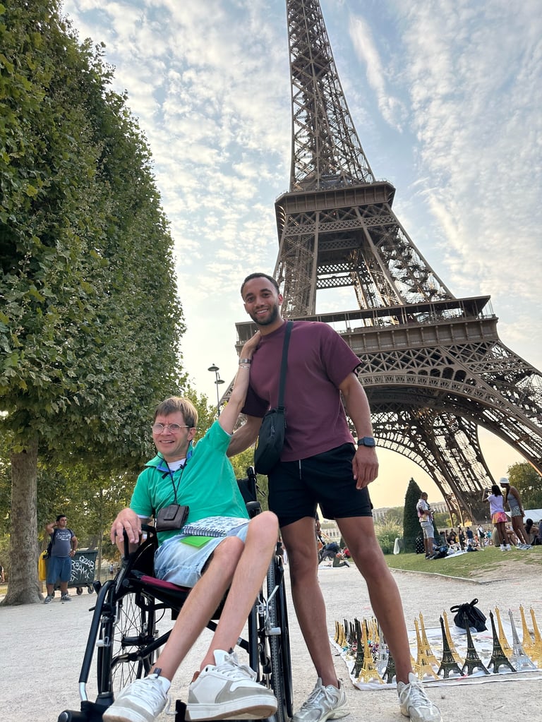 Man pushing woman in wheelchair with Eiffel Tower and tree-lined path in background