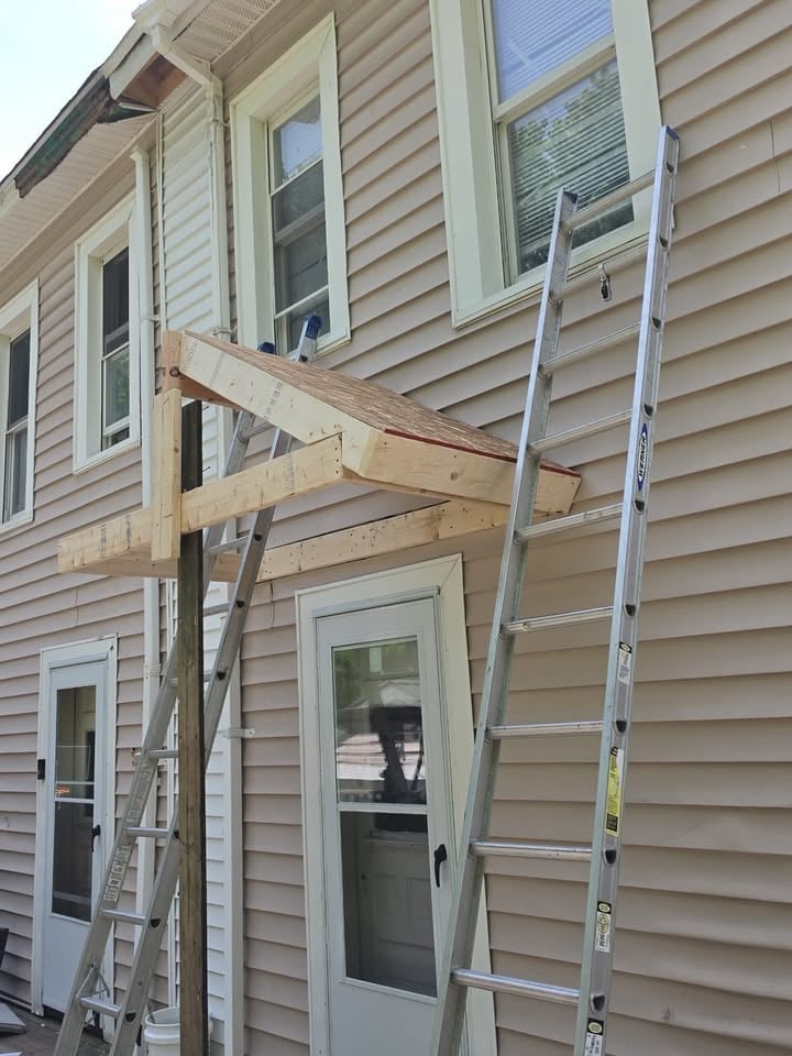 Wooden beams and metal ladders leaning against the side of a beige house under construction or renovation