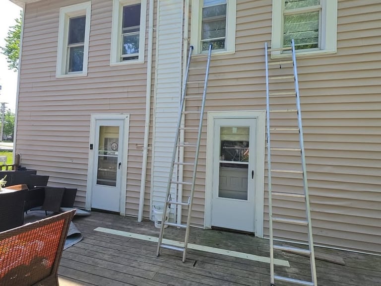 Side view of a house with tan siding, two white doors, and two leaning ladders against the exterior wall