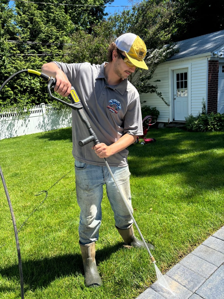 Worker in yellow hard hat and gray uniform holding a coiled hose while standing on a residential lawn