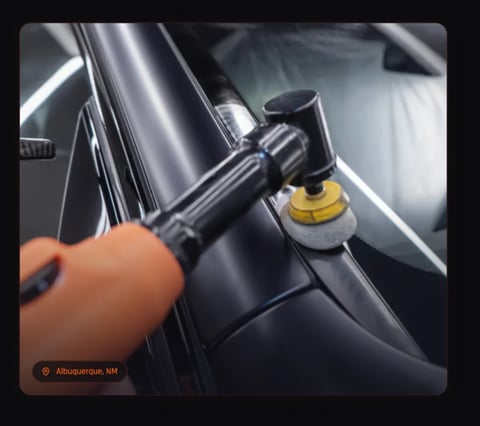 Person using a polishing tool on a black cars hood with a yellow foam pad attachment