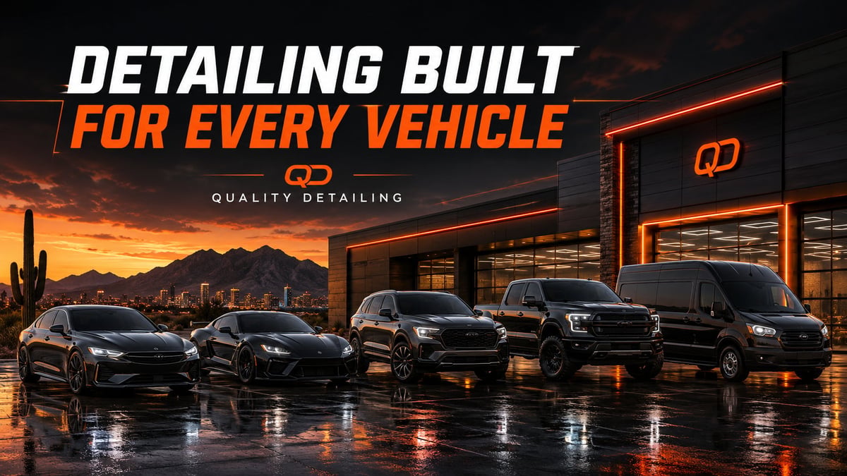 Row of five black luxury vehicles lined up at night with orange neon-lit detailing shop storefront and desert mountains sunset in background