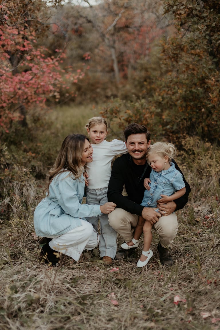 Family of four posing together outdoors among autumn foliage and trees