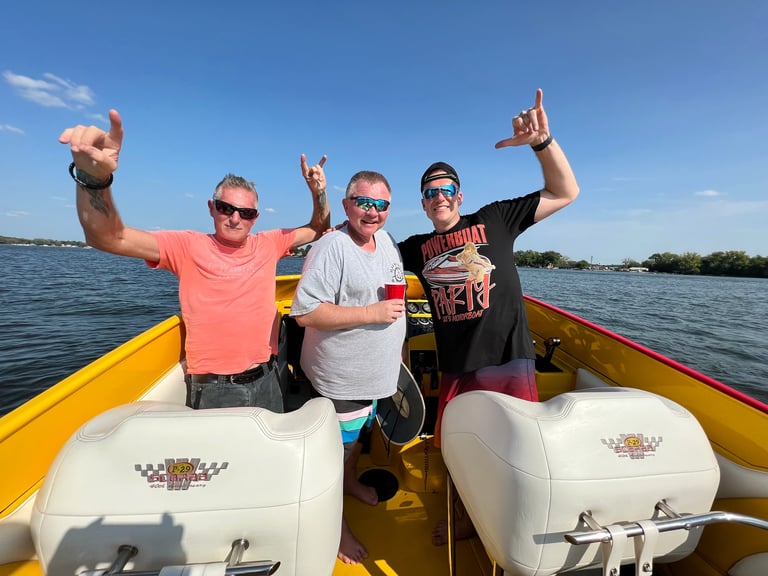 Four men in sunglasses making peace signs on a yellow speedboat in clear water under blue sky
