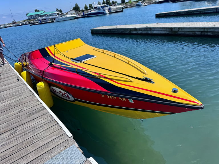 Colorful Scarab speedboats docked bow-together at a wooden pier with calm blue water and a residential marina in the background