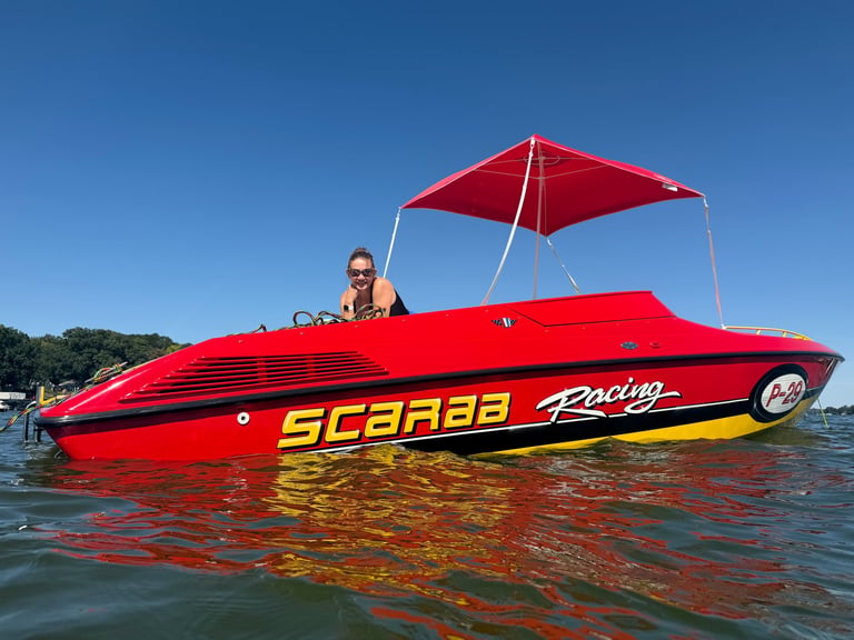 The red P-29 with SCARAB Racing graphics and its canopy up, a woman leaning on the windshield and smiling from the cockpit under a clear blue sky