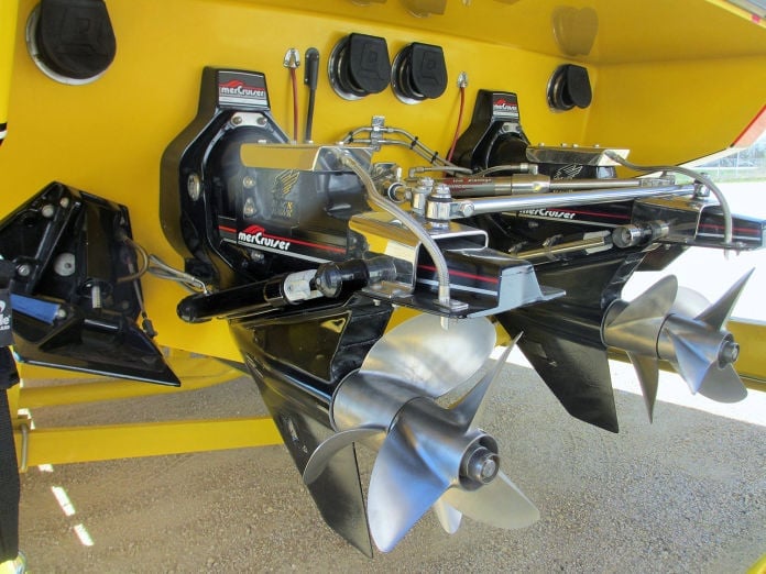 Stern of a yellow boat showing twin Mercury Racing outdrives with polished stainless steel four-blade propellers