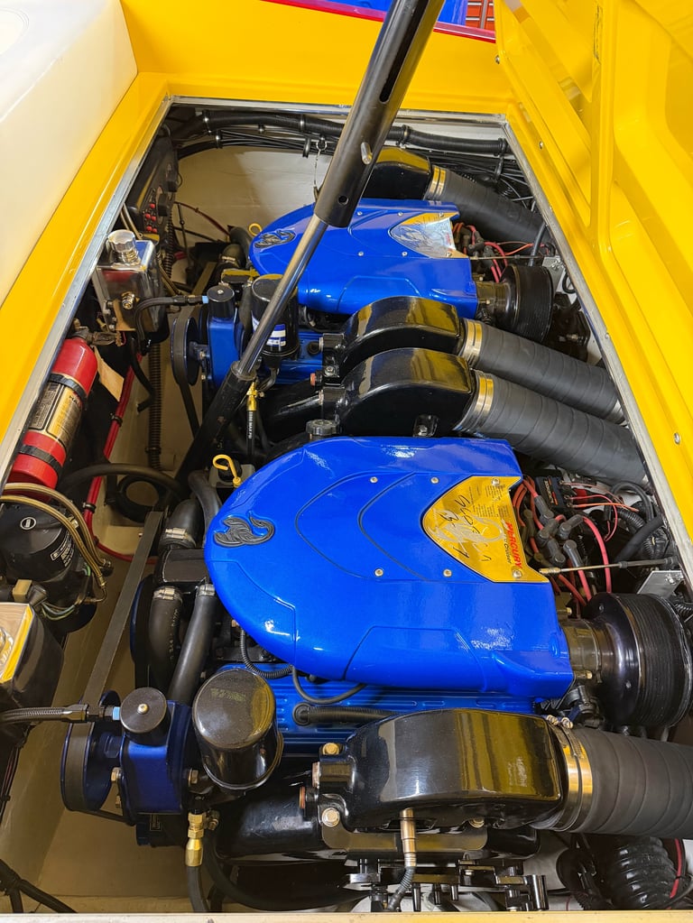 The hood up on the yellow car showing the twin blue superchargers and black intake components, red fire extinguisher mounted in the corner