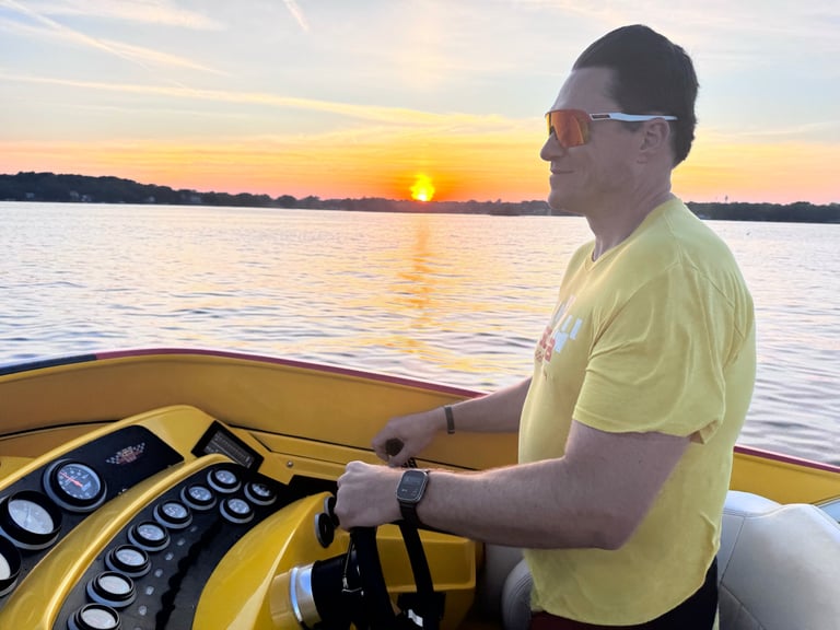 Man in yellow shirt at boat helm during sunset over calm water