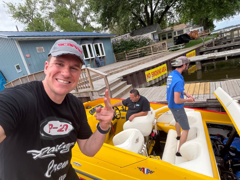 Man in cap smiling at camera on yellow speedboat docked at waterfront facility with other boats visible