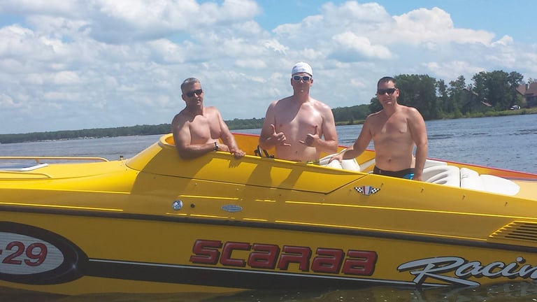 Four shirtless men in a yellow speedboat on calm blue water under partly cloudy sky