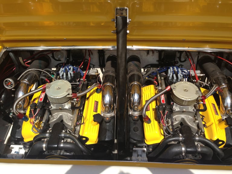 Twin yellow V8 engines with chrome manifolds and components in a gold-colored engine bay with center divider