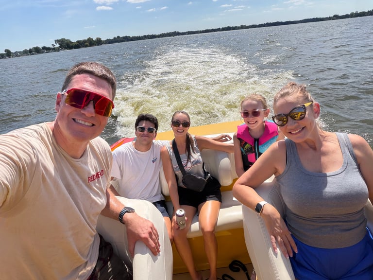Five people on a motorboat smiling at the camera with wake behind them on a sunny day