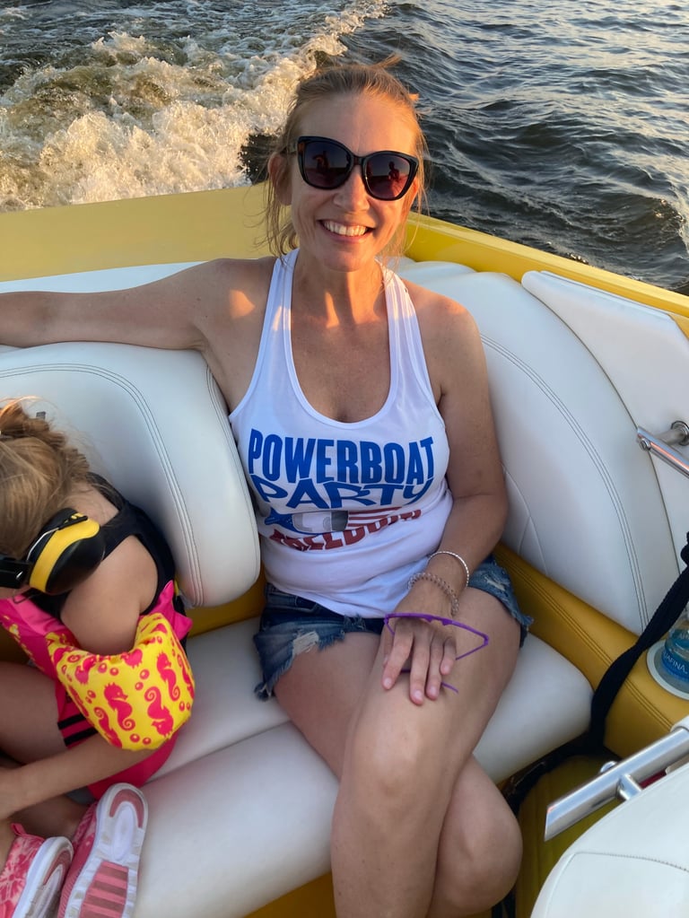 Woman in Powerboat Party tank top and sunglasses seated in a yellow speedboat with a child beside her, wake visible behind