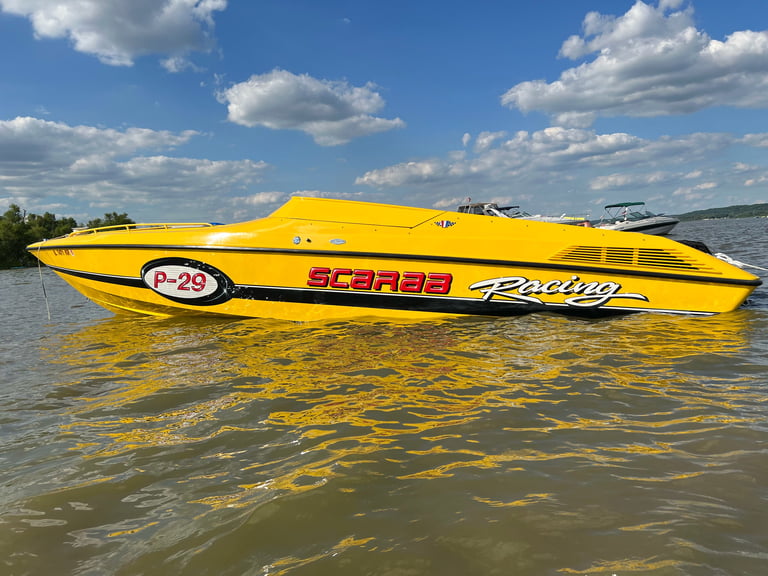 Bright yellow speedboat with Scarab branding and P-29 designation floating on calm water under blue sky with white clouds
