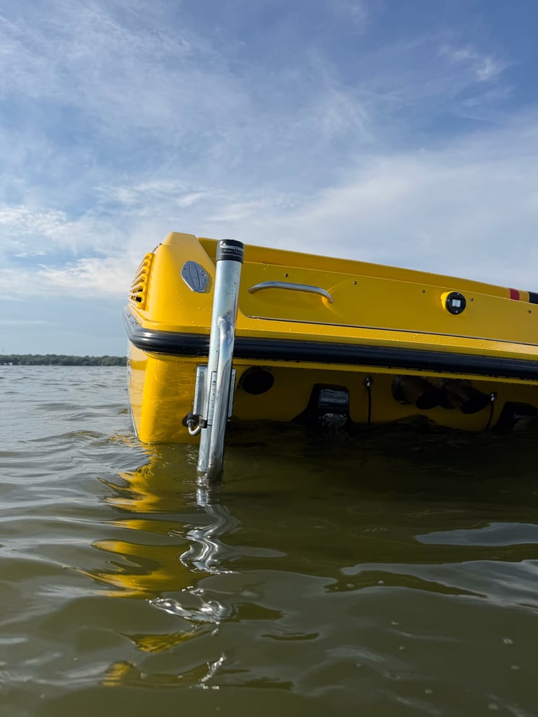 Transom view of the P-29 floating in shallow water showing the black rub rail, Mercury drive, and the stainless steel 4-step boarding ladder deployed at the swim platform