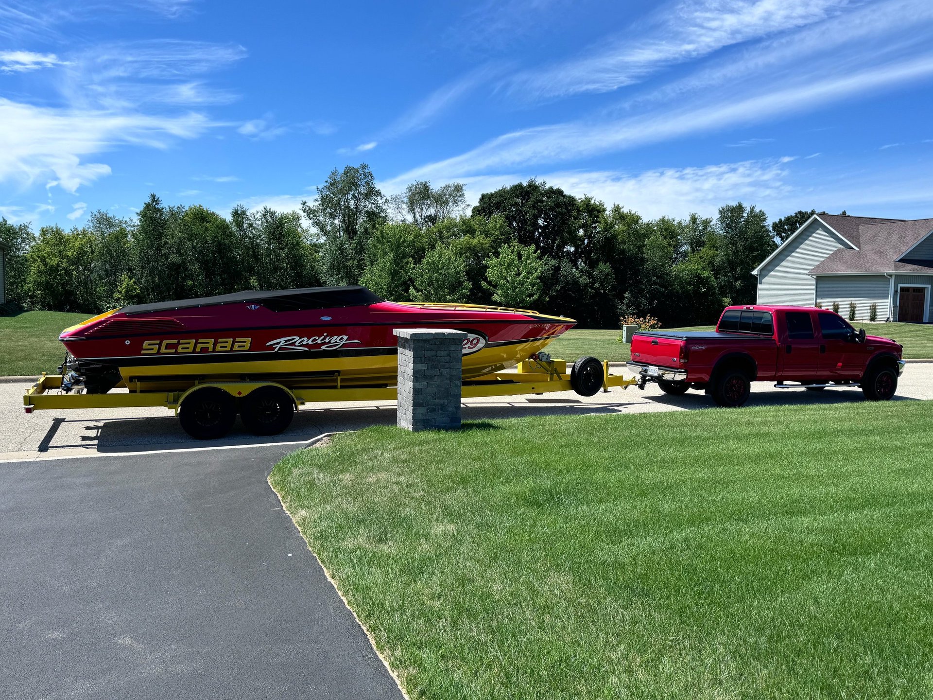 Side-by-side shot of the red F-250 hitched to the yellow Scarab P-29 trailer with the red-and-yellow boat on top, parked on a residential street with the lawn and trees behind