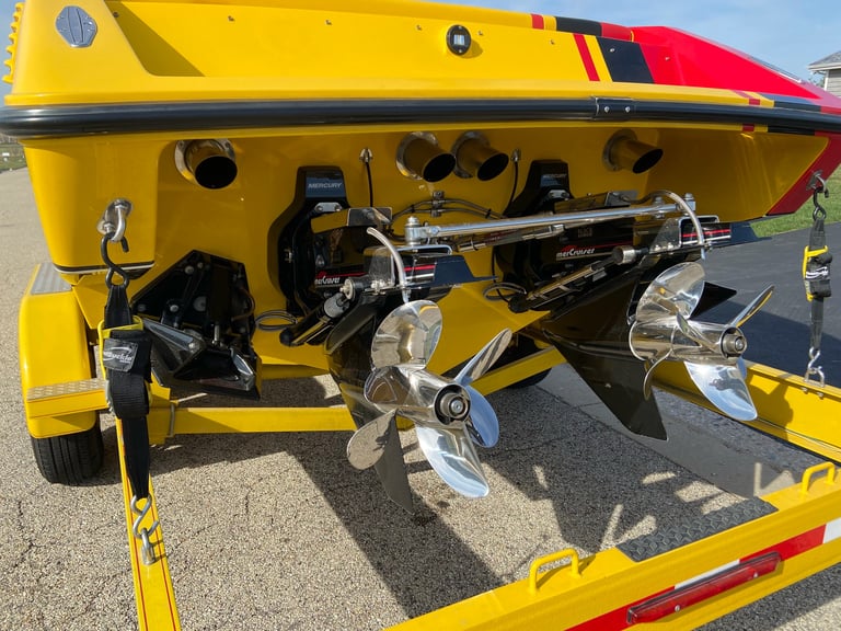 Custom-built engine bay at an outdoor car show, yellow and red tube frame carrying twin carbureted V8s with chrome valve covers on the trailer