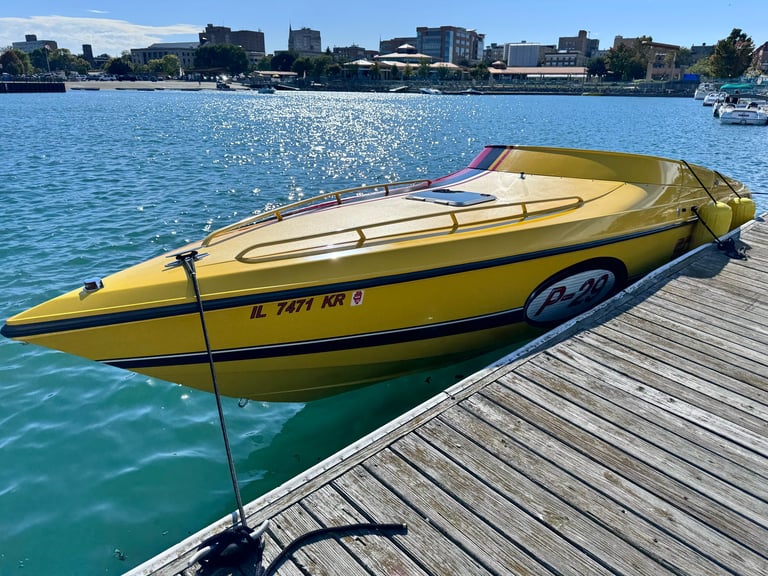 Bright yellow Scarab P-29 tied at a wooden dock with the sun glinting off blue water and waterfront buildings in the distance
