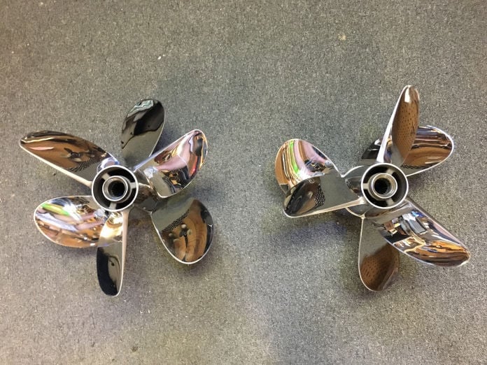 Pair of polished stainless steel four-blade Mercury Racing propellers on a concrete floor