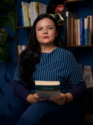 Psic. Miriam Rodríguez, especialista en acompañamiento emocional femenino, sosteniendo un libro frente a una estantería