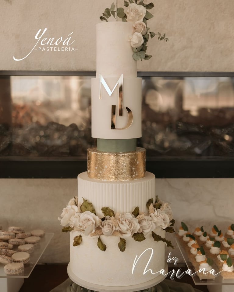 Pastel de boda de tres pisos en color blanco con detalles dorados, rosas crema y diseño geométrico moderno exhibido en la pastelería