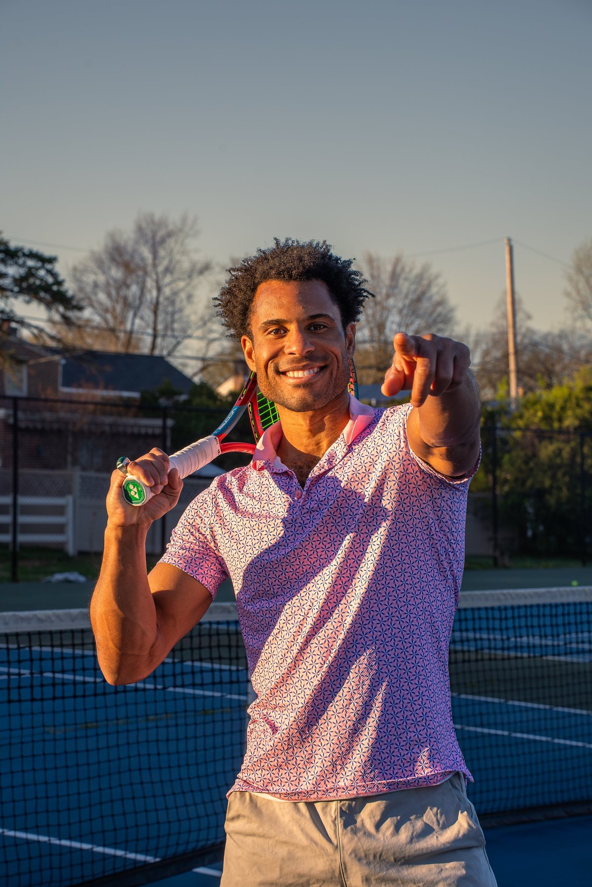 Man holding tennis racket and medal smiling on outdoor tennis court at sunset