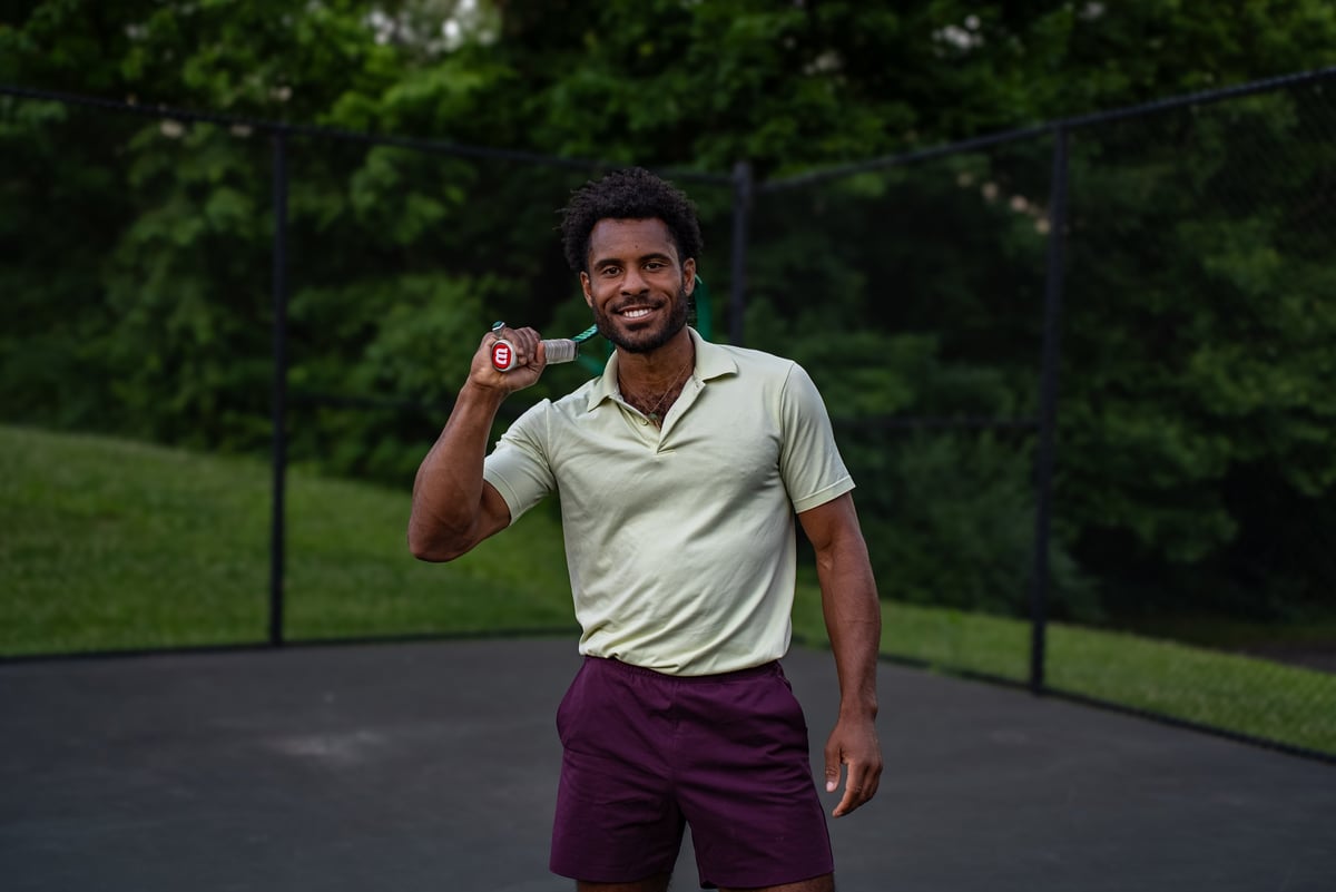 Man in light green polo and burgundy shorts holding a ring against a blurred green outdoor background