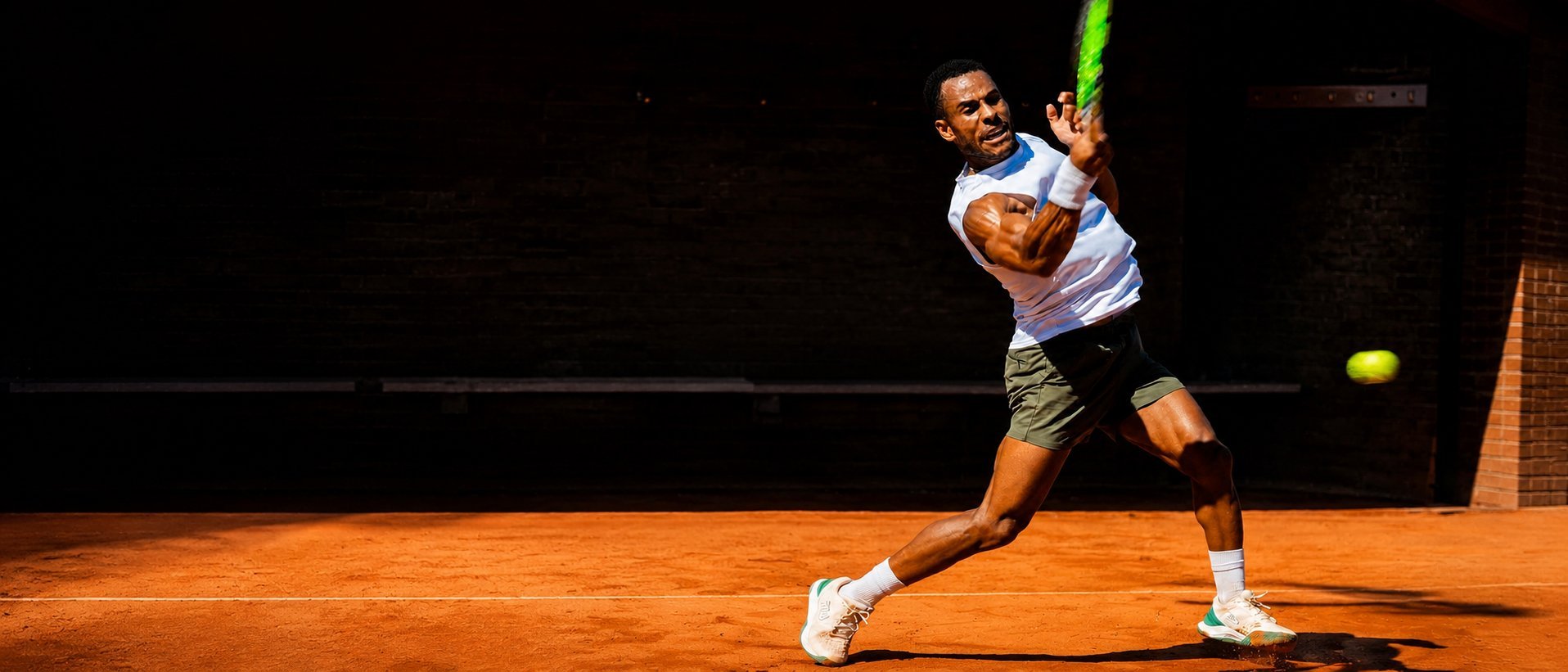 Male tennis player hitting a forehand shot with a green racket on an orange clay court during a match
