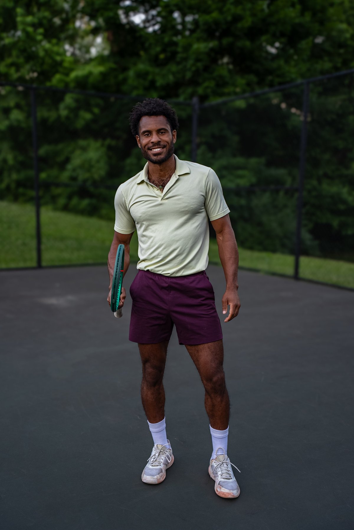 Man in casual sportswear holding a tennis racket on an outdoor tennis court with green trees in background