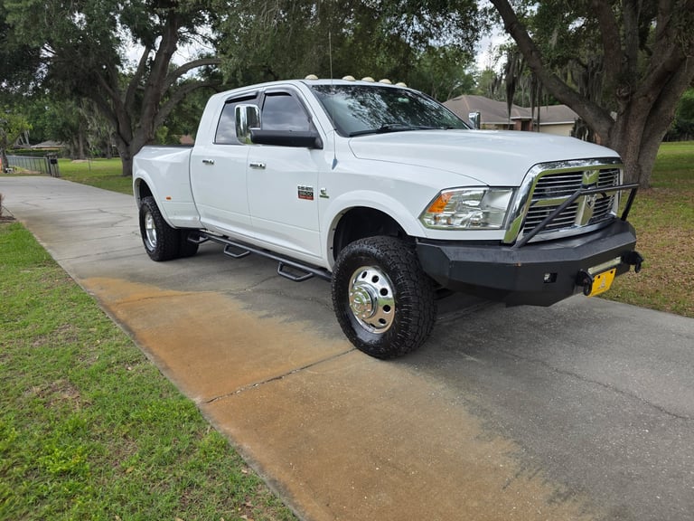White Dodge Ram pickup truck with chrome grille parked in driveway with large trees in background