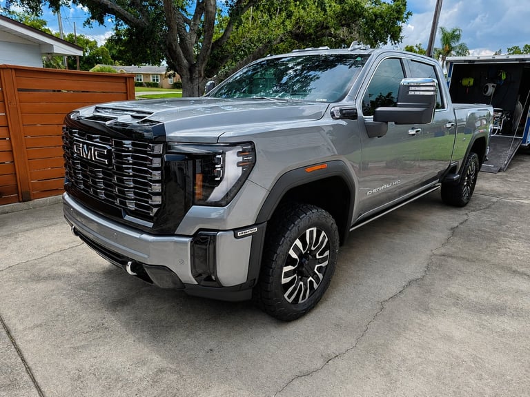 Silver GMC Sierra pickup truck parked in driveway, featuring chrome grille and alloy wheels