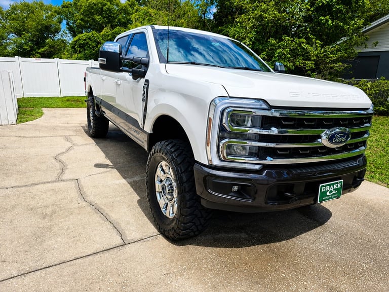 White Ford F-150 truck parked on driveway with green landscape and white fence in background