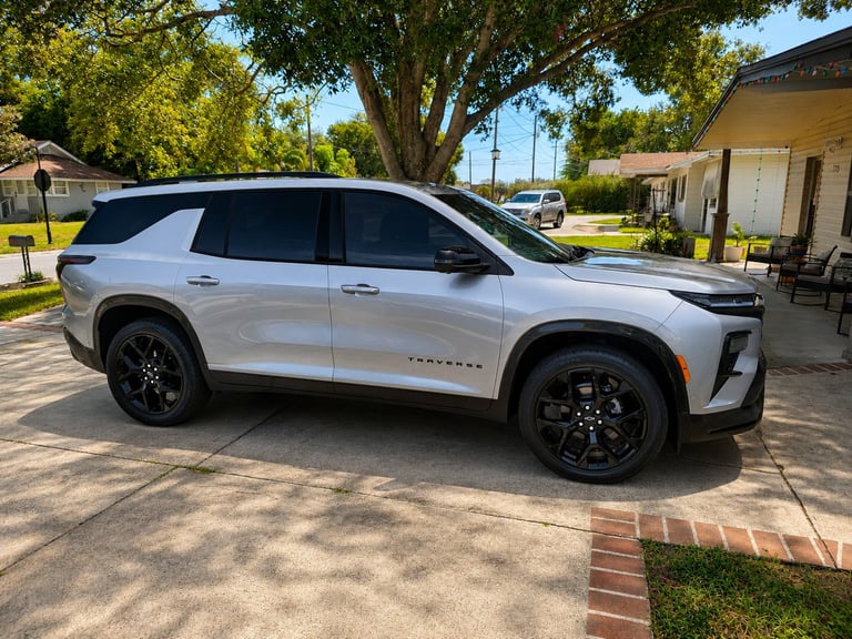 White Chevrolet Traverse SUV parked on a driveway in front of a house with large trees