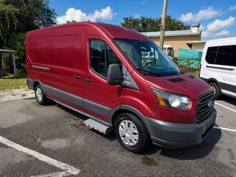 Red Ford Transit van parked in a lot with white vehicles and trees in the background