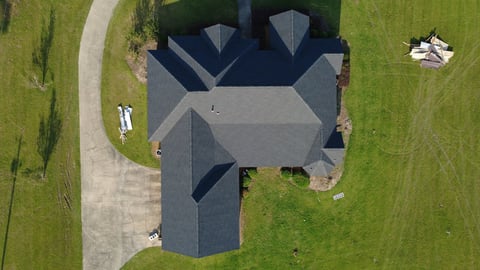 Gray residential home with dark asphalt roof surrounded by green lawn