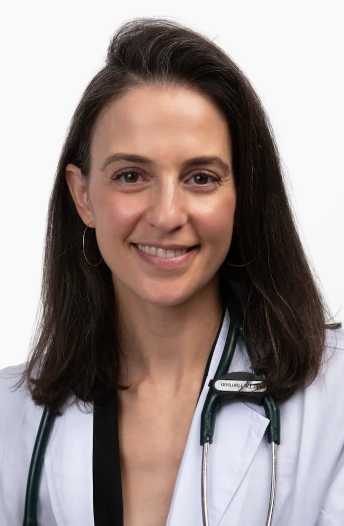 Professional headshot of a female healthcare provider wearing a white coat and stethoscope, smiling at the camera against a white background