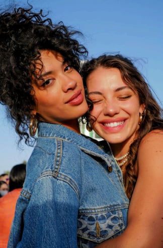 Two young women posing together outdoors against a blue sky, smiling at the camera, one wearing a denim jacket