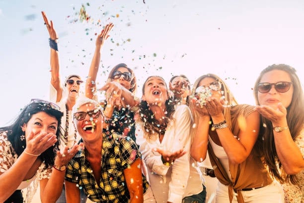Group of women celebrating outdoors, throwing confetti in the air with joyful expressions and raised hands