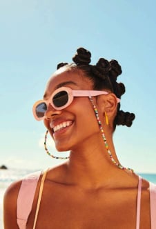 Woman wearing oversized white sunglasses and decorative hair clips smiling outdoors against a blue sky