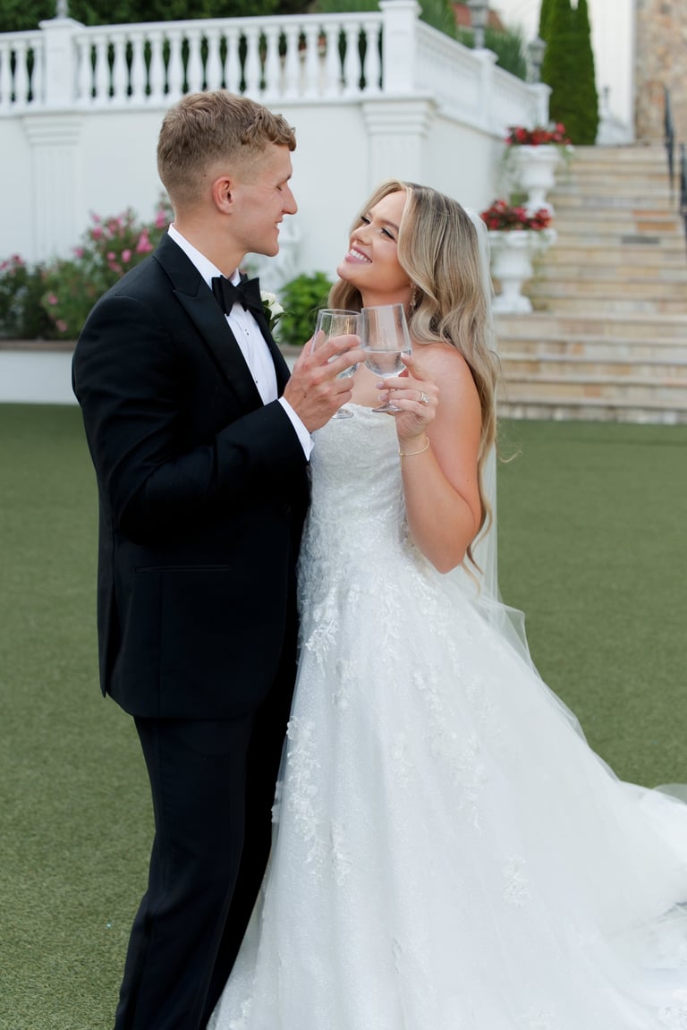 Bride and groom toasting with champagne glasses on a manicured lawn at a luxury estate wedding venue