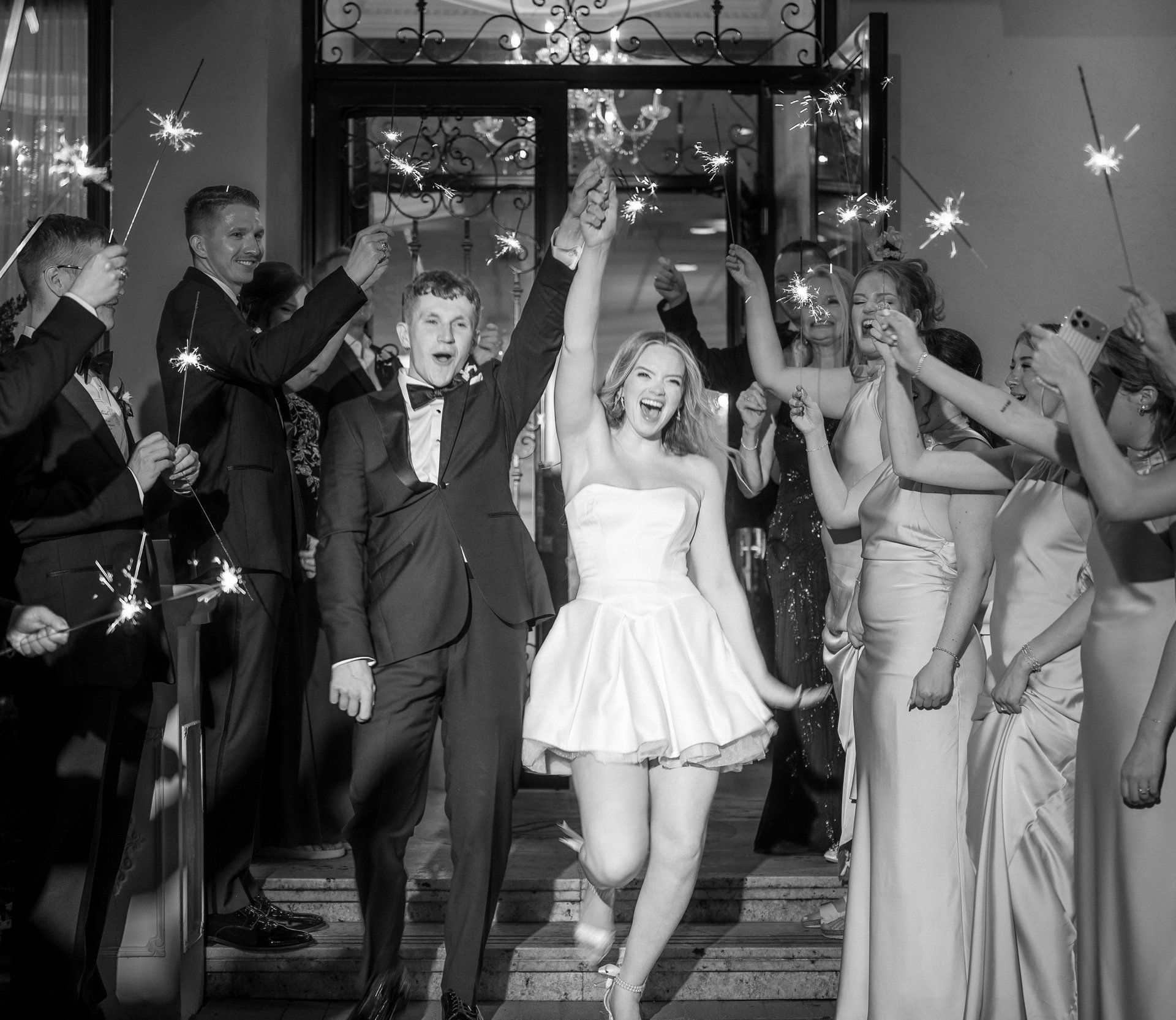 Black and white photo of newlyweds walking down building steps surrounded by wedding guests throwing confetti