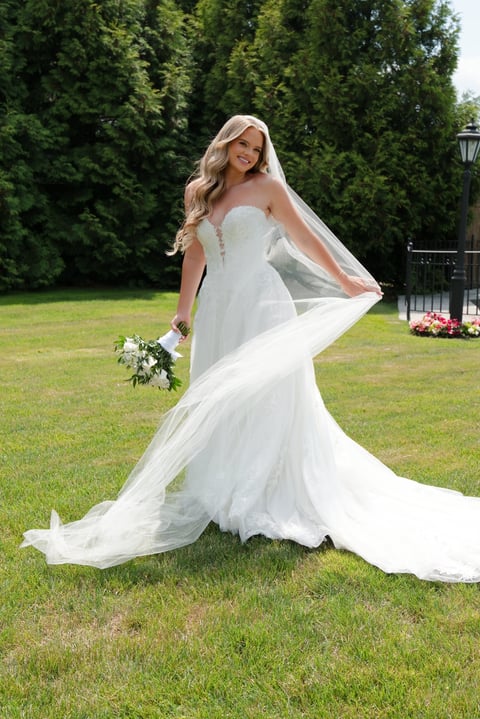 Bride in white strapless wedding dress with flowing veil and bouquet posing in garden setting