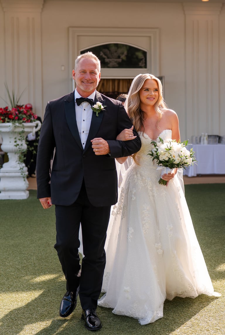 Bride and groom walking together on lawn at outdoor wedding ceremony venue with elegant white colonial architecture and red floral arrangements
