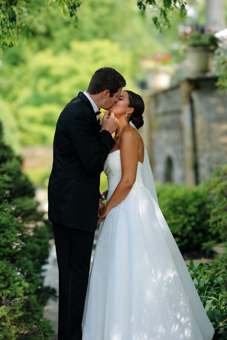 Bride and groom kissing in a garden pathway, groom in black suit and bride in white wedding dress