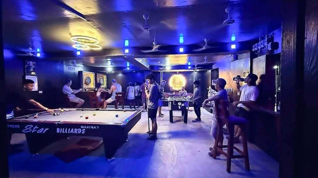 Indoor billiards lounge with blue neon lighting, pool tables, and patrons socializing in a dark modern game room